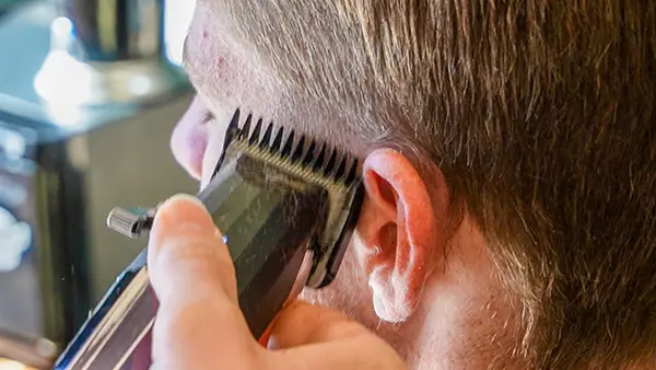 A close-up shot of hair clippers gently resting against a customer's head.